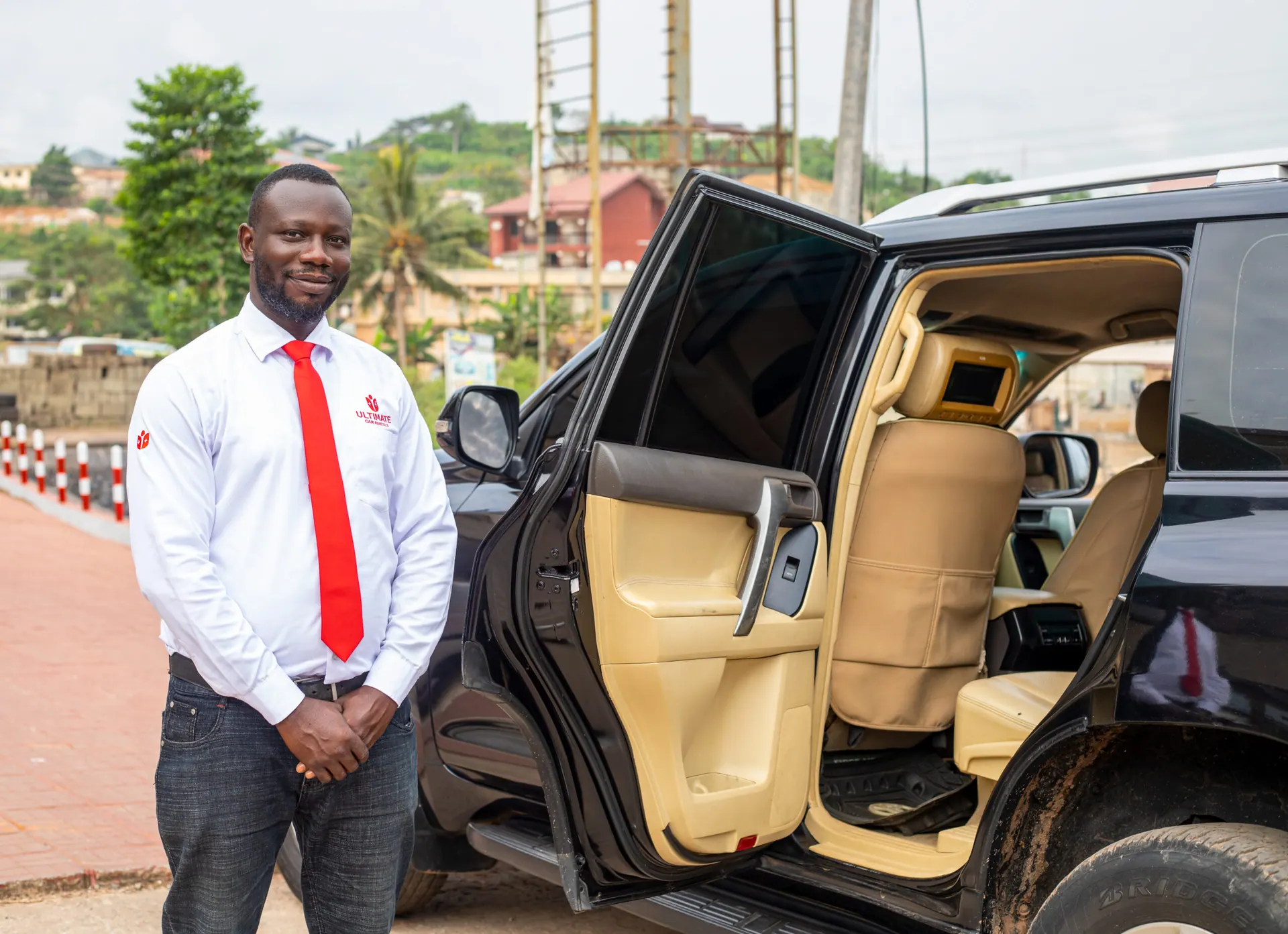 Professional Ultimate Car Rentals chauffeur standing by a Land Cruiser Prado